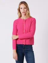 Cardigan de punto color fucsia, con escote a la base, cierre frontal con botones metálicos dorados y terminaciones desflecadas. Presenta bolsillos simulados en la parte delantera y mangas largas.
