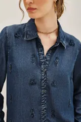 Camisa de denim azul oscuro con cuello clásico, cierre frontal de botones y mangas largas. Presenta un delicado bordado de motivos florales y vegetales realizado con cuentas y canutillos en tono azul marino.