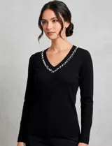 Buzo de tejido fino en color negro, con escote en V decorado con perlas y strass bordados. Presenta mangas largas con puños en punto rib y ruedo con terminación acanalada.