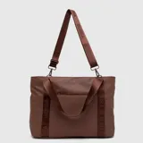 Tote bag color marrón, con diseño minimalista y logo de la marca grabado en el frente. Cuenta con doble asa de mano y una correa larga ajustable y extraíble, ambas con el nombre de la marca estampado. Incluye un bolsillo frontal con cierre.