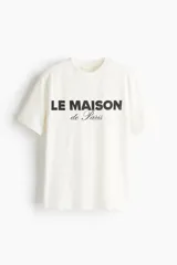 Remera de punto de algodón color blanco, con cuello redondo, mangas cortas y diseño estampado frontal con la inscripción "LE MAISON de Paris" en negro.