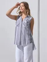 Camisa sin mangas de corte recto, con cuello clásico y escote en V. Presenta un diseño de rayas verticales en tonos lila, rosa, blanco y gris, con dos bolsillos frontales aplicados con estampado en chevron. Cuenta con cierre central de botones.