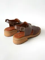 Sandalias de cuero color chocolate con suela track y taco bajo cuadrado. Poseen capellada cerrada con aberturas laterales y tira ajustable en el talón con hebilla metálica.