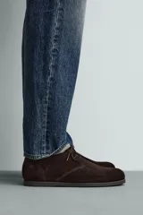 Bota de cordones tipo derby, color marrón oscuro, fabricada en piel con acabado serraje. Tiene plantilla interior de piel, horma redonda y suela fina a contraste.