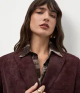 Blazer estructurado de corte sastre confeccionado en tejido sintético tipo gamuza (suede), con diseño de abotonado cruzado, solapas clásicas, bolsillos con tapa y mangas largas con botones en los puños.