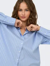 Camisa de manga larga con cuello clásico y cierre frontal de botones. Presenta un diseño de rayas verticales blancas sobre fondo azul claro, con corte holgado y puños anchos.
