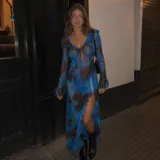 Vestido largo de microtul translúcido con estampado floral en tonos azules y marrones. Posee escote en V con lazo ajustable, mangas largas acampanadas con volados y una abertura lateral en la falda.