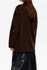 Jersey de punto color marrón con detalles de encaje negro aplicados en el hombro y lateral. Presenta cuello redondo, manga larga y corte holgado.