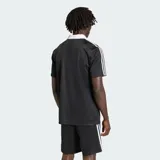 Camiseta Adidas Originals de manga corta, color negro con sutiles rayas verticales, cuello polo en V de color blanco, al igual que las líneas características de la marca en los hombros. Cuenta con el logotipo de la marca y la inscripción "adidas" en el pecho en color blanco.
