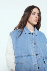 Chaleco de jean con corte oversized, diseño sin mangas, cuello camisero, cierre frontal con botones metálicos y bolsillos frontales tipo cargo.
