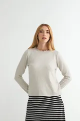 Sweater de punto color beige, de manga larga y cuello redondo con detalle de volados en el borde.