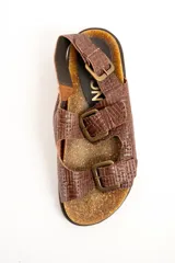 Sandalias de cuero color marrón con textura trenzada, plantilla anatómica de corcho y suela dentada. Posee tres tiras ajustables con hebillas metálicas y tira en el talón.