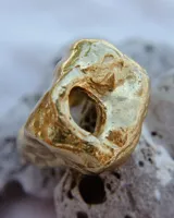 Anillo dorado con forma irregular y un agujero en el centro.