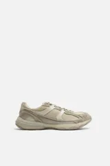 Zapatilla deportiva tipo running de color beige, con parte superior en combinación de cuero con acabado serraje y tejido transpirable. Cuenta con suela de volumen irregular y pertenece a la colección especial Origins.