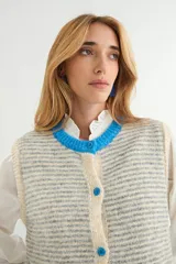 Chaleco de punto con diseño a rayas horizontales en gris y blanco. Presenta cuello redondo, bordes y bolsillos frontales con detalles en color rojo, y cierre frontal con botones rojos.