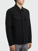 Chaqueta de estilo utilitario en color negro, con cuello camisero, cierre frontal oculto y dos bolsillos con solapa en el pecho. Presenta un diseño minimalista y funcional.