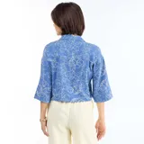 Camisa azul con estampado floral en blanco, de corte oversize, mangas tres cuartos, escote en V con cuello y detalle de nudo en el frente.