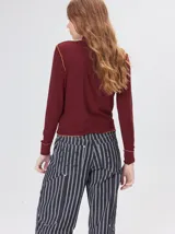 Remera de cuello alto tipo polera, confeccionada en tela rib con textura acanalada y ajuste al cuerpo. Presenta mangas largas y un pequeño bordado distintivo en la parte inferior.