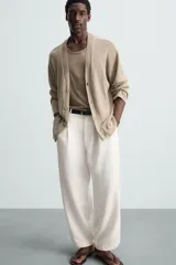 Pantalón blanco de corte relajado (relaxed fit) con pliegues frontales, bolsillos laterales y bolsillos traseros de vivo. Cierre frontal con cremallera y botón.