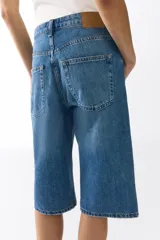 Bermuda de cinco bolsillos en denim de algodón, de tiro alto con cierre de botones y detalles de roturas.
