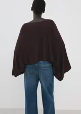 Poncho de punto asimétrico en color bordó, con diseño de capa y cuello barco de mangas amplias.