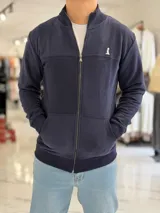 Campera azul marino de felpa con cierre frontal completo, cuello mao, bolsillos tipo canguro y logo bordado en el pecho.