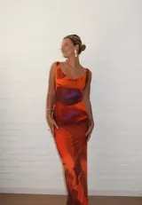 Vestido largo ajustado de microtul, color naranja con degradado a tonos rojizos y detalles en tonos morados/fucsia en la zona del torso. Presenta escote en V con efecto drapeado y tirantes anchos.