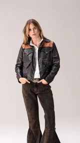 Campera de cuero negra de corte recto, con detalles en cuero marrón tostado en los hombros y canesú. Cuenta con múltiples bolsillos frontales con solapa, cierre de botones a presión y tachas metálicas decorativas.