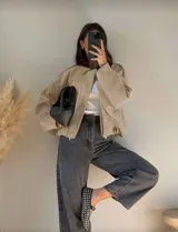 Chaqueta tipo bomber de calce holgado, confeccionada en gamuza color beige. Presenta cuello camisero, cierre frontal, mangas amplias y largo a la cintura.