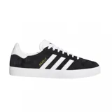 Championes urbanos Adidas modelo Gazelle Adv, color negro con las icónicas tres tiras laterales y talón en blanco. Confeccionados en gamuza, cuentan con suela de goma blanca y el nombre del modelo en letras doradas en el lateral.