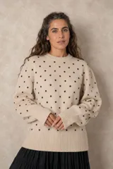 Buzo de punto color beige con estampado de lunares negros en relieve, cuello redondo y mangas largas con puños acanalados.