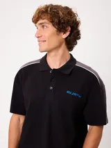 Remera polo gris melange de ajuste holgado, con cuello y cierre frontal de botones. Presenta detalles en azul marino y blanco en los hombros y mangas, y el logo de la marca bordado en el pecho.