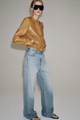 Campera bomber de cuero 100% color tostado de la ZARA WOMAN COLLECTION, con cuello redondo, manga larga, bolsillos delanteros ribeteados y cierre frontal con botones metálicos en relieve. Presenta elástico fruncido en el dobladillo inferior.