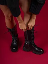 Bota de caña media color negro, con cordones y suela track.