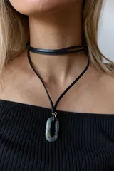Gargantilla de tiento de cuero negro con dije colgante de piedra natural ovalada y argolla metálica dorada.