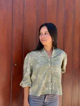 Camisa de corte holgado en color verde con estampado floral lineal en tono crema. Presenta cuello mao, cierre frontal con botones y mangas tres cuartos con puños elásticos.