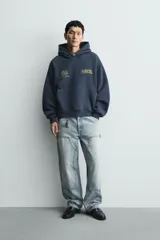 Sudadera tipo hoodie de corte relajado en color azul oscuro con efecto lavado. Presenta capucha, manga larga, bolsillo frontal tipo canguro y detalles estampados en color dorado en el pecho.