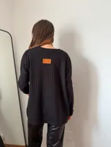 Sweater de morley texturado color negro, de corte relajado y holgado, con mangas largas y tajos laterales en el ruedo. Presenta una etiqueta de cuero sintético en la parte superior de la espalda.