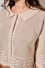 Cardigan de algodón peinado color beige, con cuello camisero, cierre frontal de botones y detalles de textura en crochet con diseño de flores. Mangas tres cuartos y diseño corto.