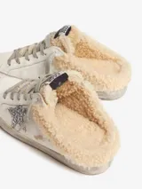 Zapatilla deportiva de cuero blanco con cordones grises, detalle de estrella plateada con glitter en el lateral y forro de lana color crema.