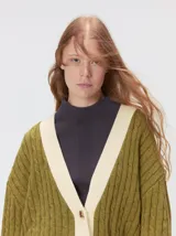 Cardigan de tejido de punto con diseño de ochos, corte oversize y mangas largas con puños acanalados. Presenta un escote en V con solapas en contraste, cierre frontal con botones y dos bolsillos delanteros con bordes en contraste. El diseño incluye detalles de rayas en los puños y en el ruedo.