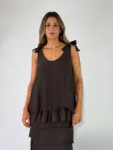 Top marrón oscuro de viscosa, sin mangas, con escote redondo y tirantes ajustables mediante lazos en los hombros. Presenta un diseño holgado con detalle de volados en el borde inferior.