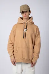 Buzo canguro color ocre con capucha y cordones negros, de corte oversize y confeccionado en tela de algodón friza con teñido artesanal y estampa circular en el pecho.