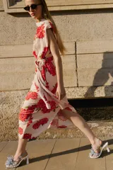 Vestido midi de color beige con estampado floral en tonos rojos y fucsias, con cuello fluido, manga sisa y cinturón del mismo tejido.