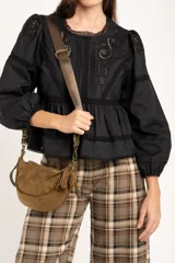Blusa negra de algodón con diseño de broderie y calados en el pecho y hombros. Presenta corte oversize, mangas largas con puños y un detalle de volado en la cintura.