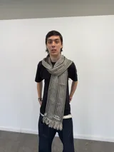 Bufanda larga de tejido trenzado con diseño de cuadros en tonos beige, marrón, negro y blanco. Presenta flecos en los extremos, una grifa de goma con logo en una punta y una etiqueta tejida con logo en la otra.