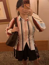 Camisa negra de popelina, con diseño cruzado y cordones laterales estilo corsé, cuello clásico, mangas abullonadas y gran estampado floral en el frente.