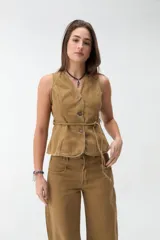 Chaleco de denim color beige, sin mangas, con escote en V, cierre frontal con botones y lazo ajustable en la cintura.