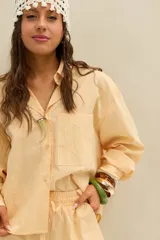 Camisa amarilla de manga larga con diseño de rayas finas, corte oversize, cuello camisero, cierre frontal con botones y bolsillo ojal en el pecho.