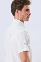 Camisa de manga corta confeccionada en tejido piqué de algodón, color blanco, con cuello con botones y cierre frontal abotonado.